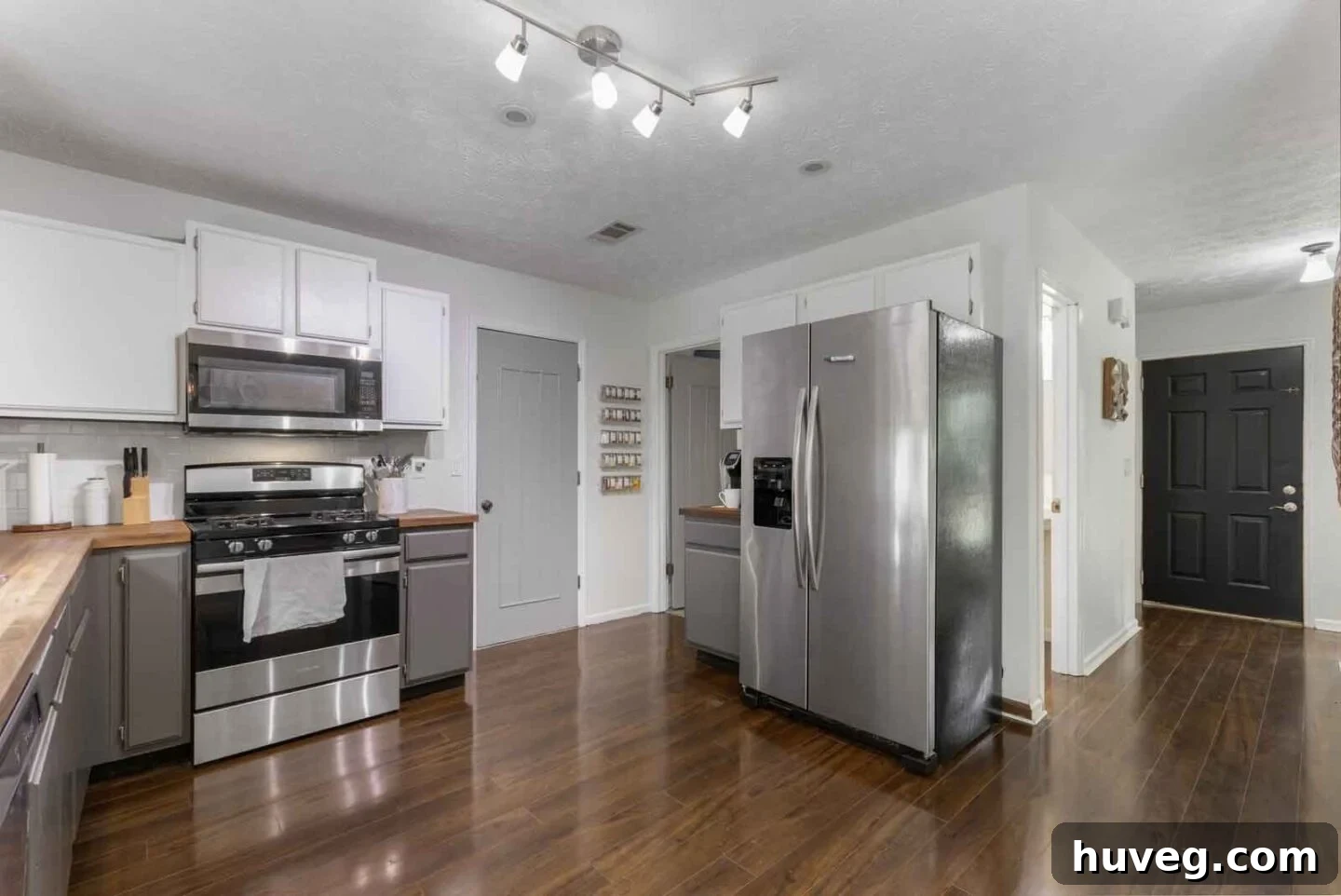 kitchen view to laundry room with two tone white and gray cabinets butcher block counters and dark wood floors