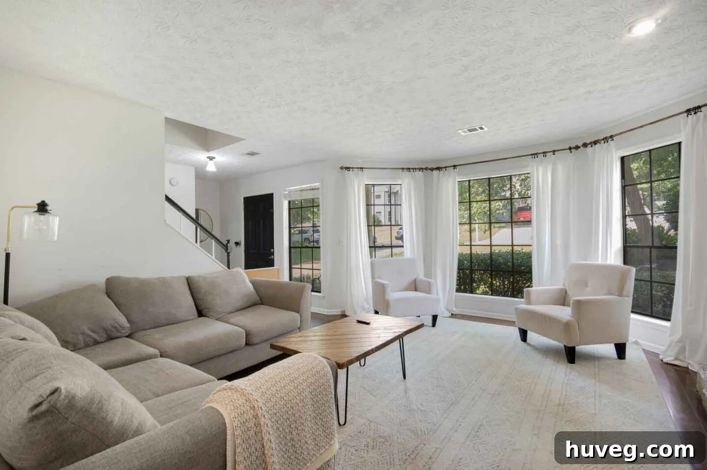 living room with gray sectional white walls and white curtains in front of bay window