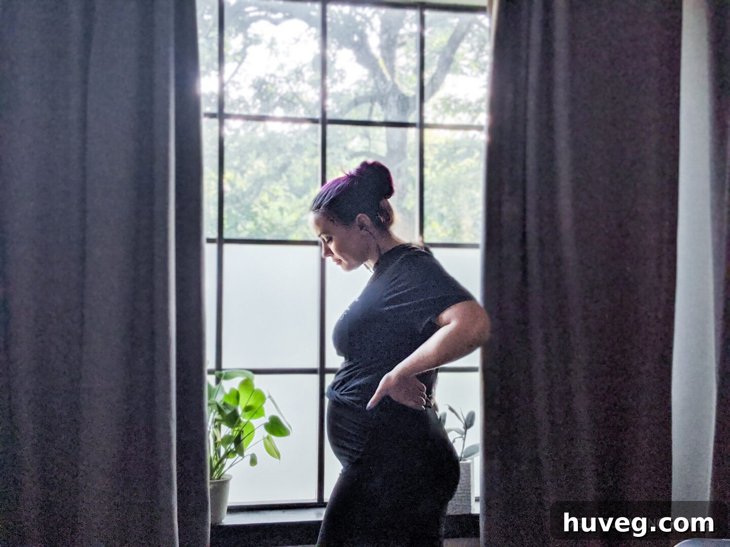 standing in the window with pregnancy bump and houseplants