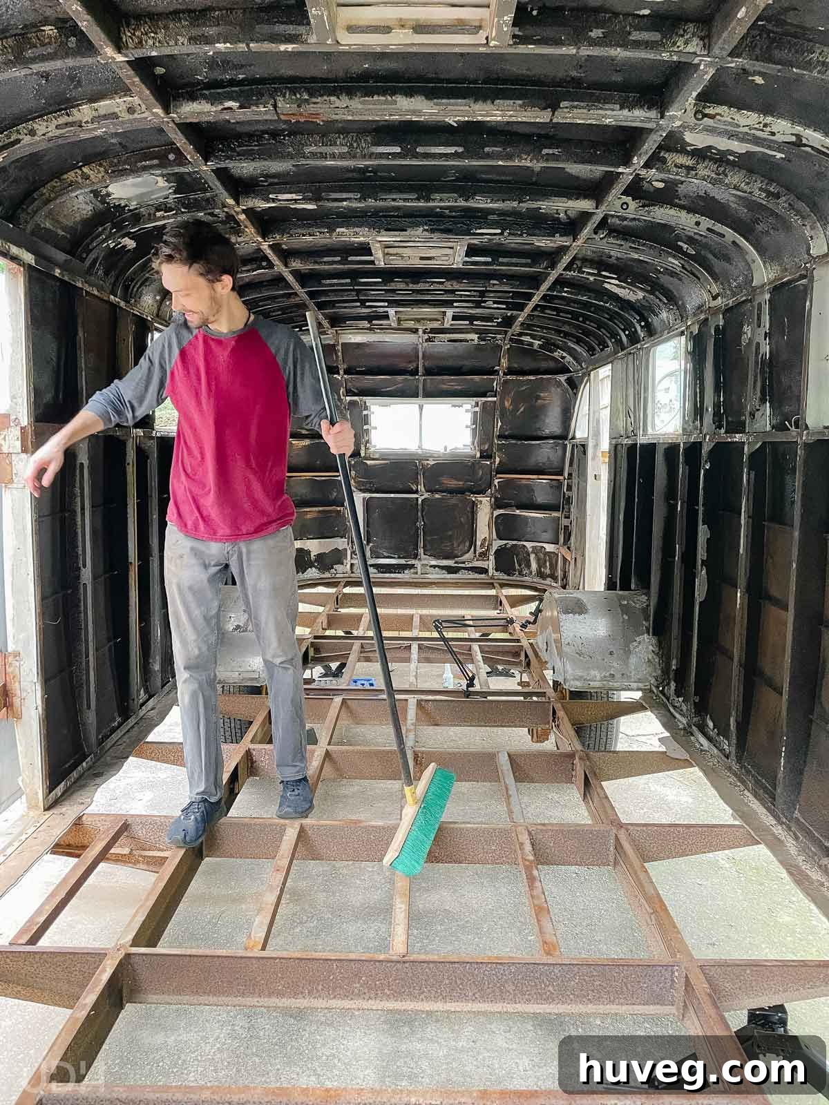 The completely gutted interior of Ruby's Revival, with the subfloor torn out and Kyle sweeping debris, revealing the extensive renovation.