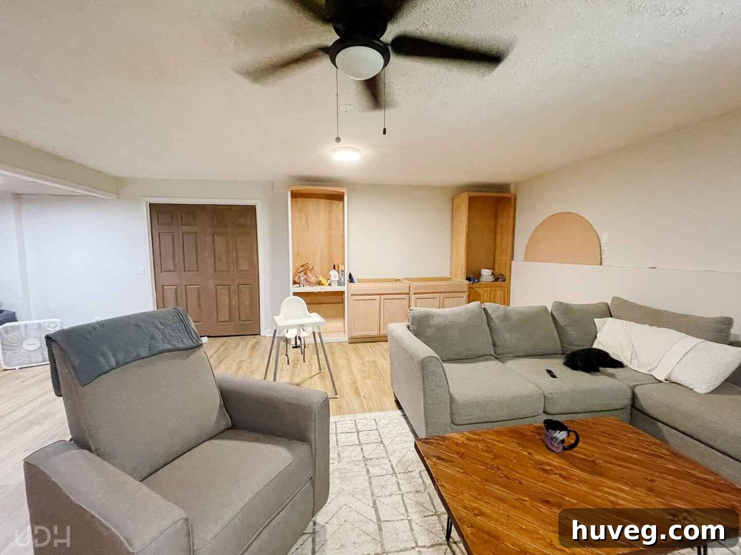 Mid-remodel basement apartment with a cozy couch, coffee table, functional kitchenette, and a charming rocking chair.