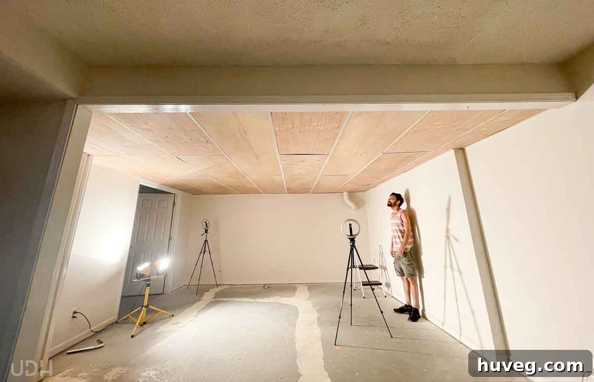 Kyle standing in an empty basement room, featuring a low wooden ceiling and a spotlight in the corner, awaiting transformation.