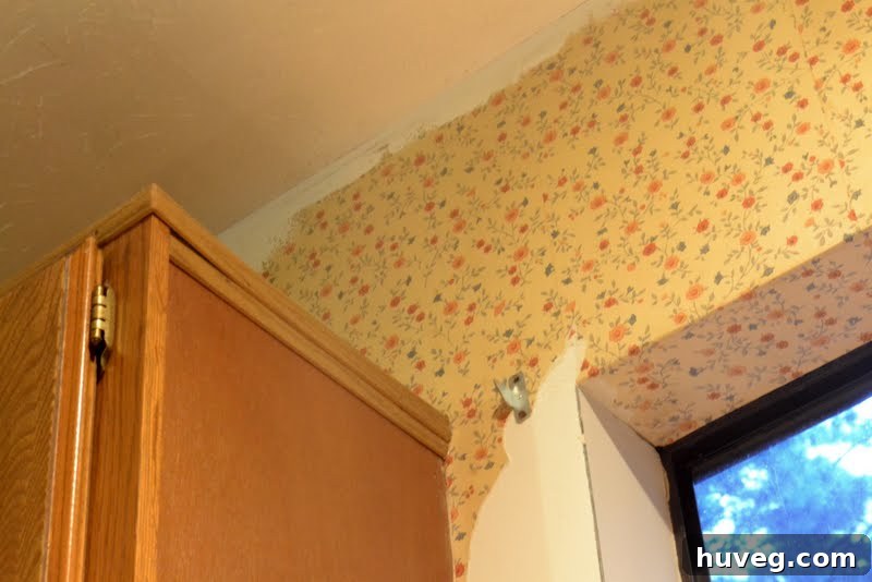 A view of a kitchen under renovation, showing exposed walls and the initial stages of a remodel, with a person's hand visible and a sense of ongoing work.