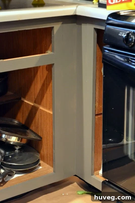 Progress shot of kitchen lower cabinets painted gray, featuring a sink area partially covered with drop cloths and renovation tools