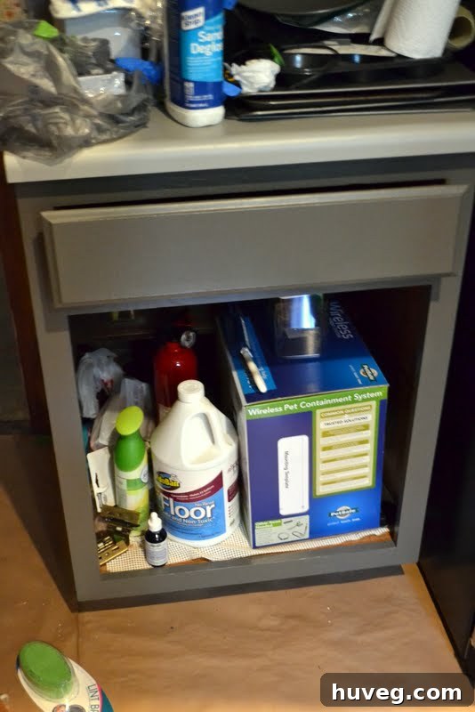 Kitchen renovation in progress, showing painted gray lower cabinets, clutter on countertops, and tools scattered around