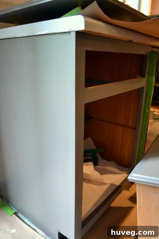 Overhead view of a kitchen in renovation, showing painted lower cabinets, an open fridge, and various items on the floor and counters