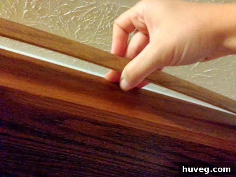 Close-up of hands gently pulling away a small piece of old, decorative molding from the top of a kitchen cabinet