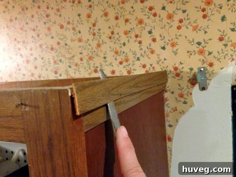 Close-up image showing the back of a removed piece of cabinet molding, caked with thick layers of dirt and kitchen grime