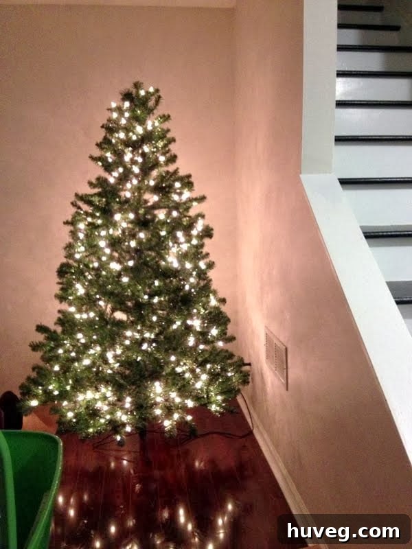 A beautifully lit artificial Christmas tree stands in a bright living room, partially decorated.