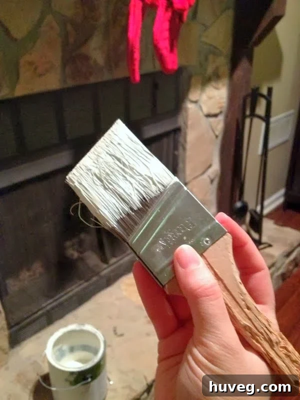 Close-up of a well-used paint brush with a chewed handle, resting near a freshly painted white fireplace surround.