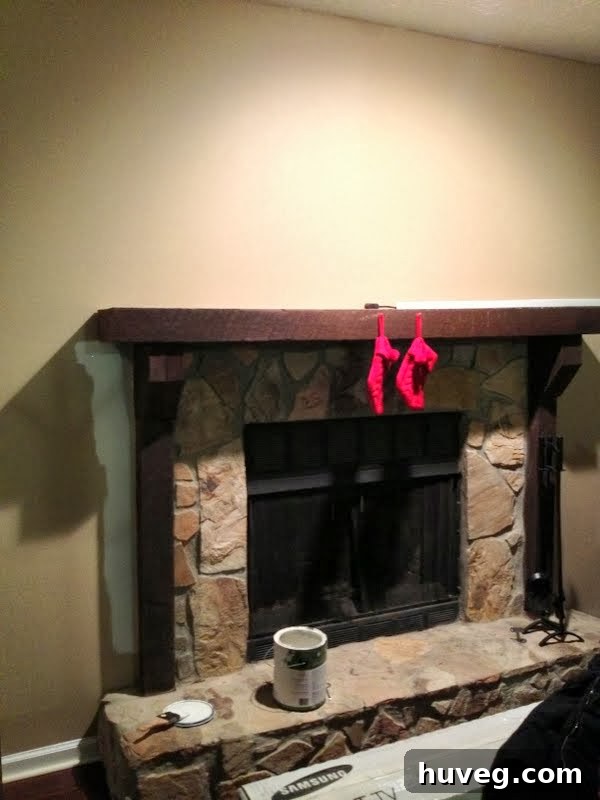 A dark living room showing a freshly painted white fireplace and mantel, with a few small red Christmas stockings hanging. The room appears dim, highlighting the need for more light.