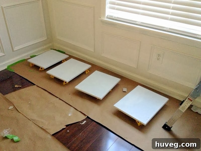 Several cabinet doors propped up on yellow paint pyramids, showcasing a freshly painted white finish in a brightly lit room.