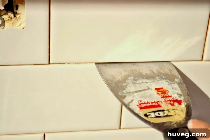 Cleaning excess thinset from tile gaps with a putty knife