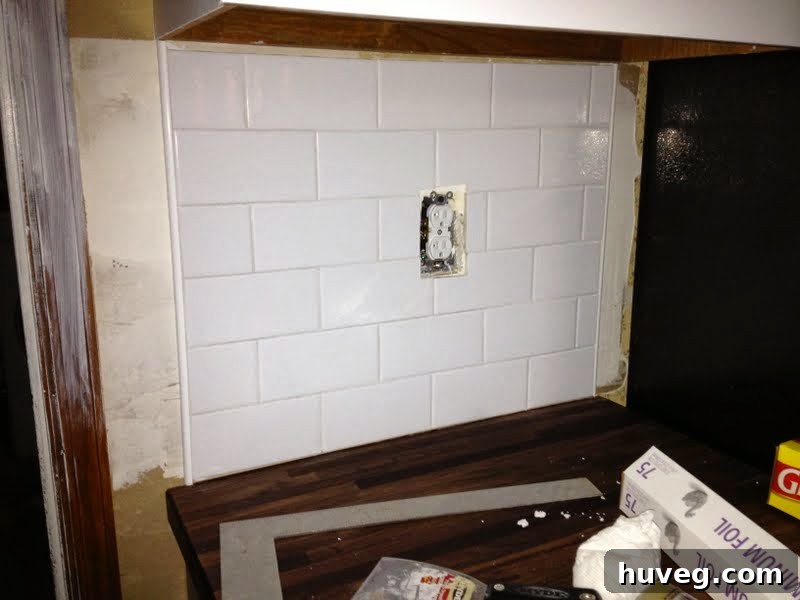 Awkwardly lit corner of a kitchen backsplash with partially applied grout, demonstrating initial progress on a DIY project.