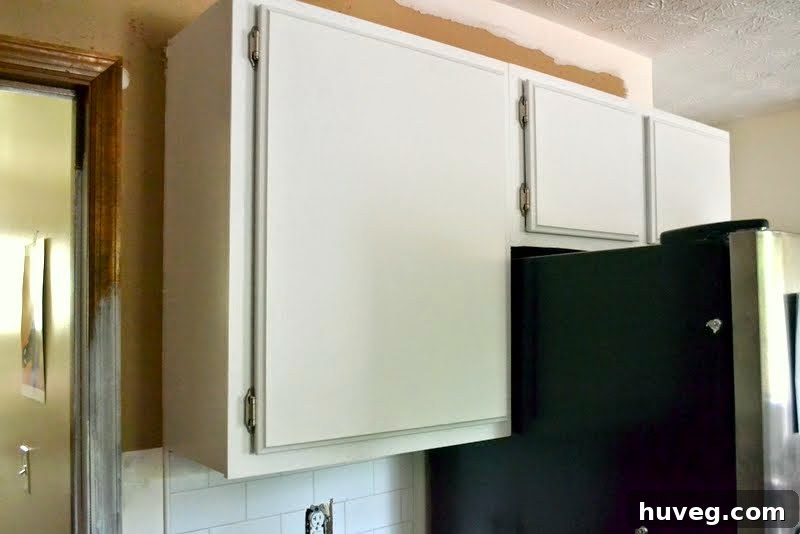 Newly installed white upper kitchen cabinet doors creating a clean, modern look next to a refrigerator