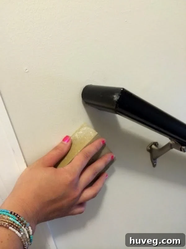 Using a sanding sponge to remove scuff marks from the wall after handrail installation