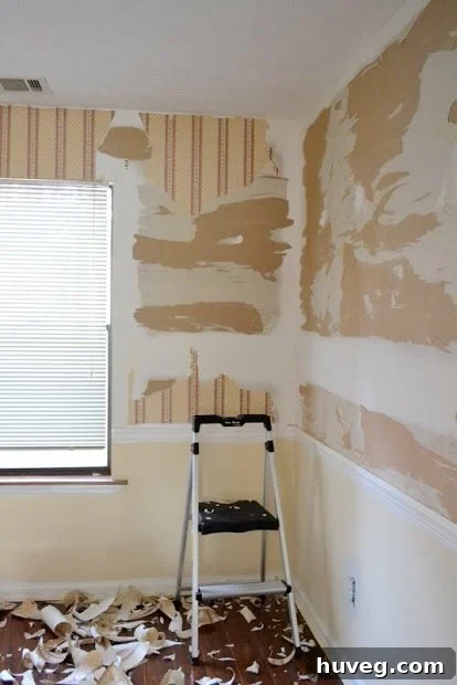 Wall in progress of wallpaper removal, showing damaged drywall