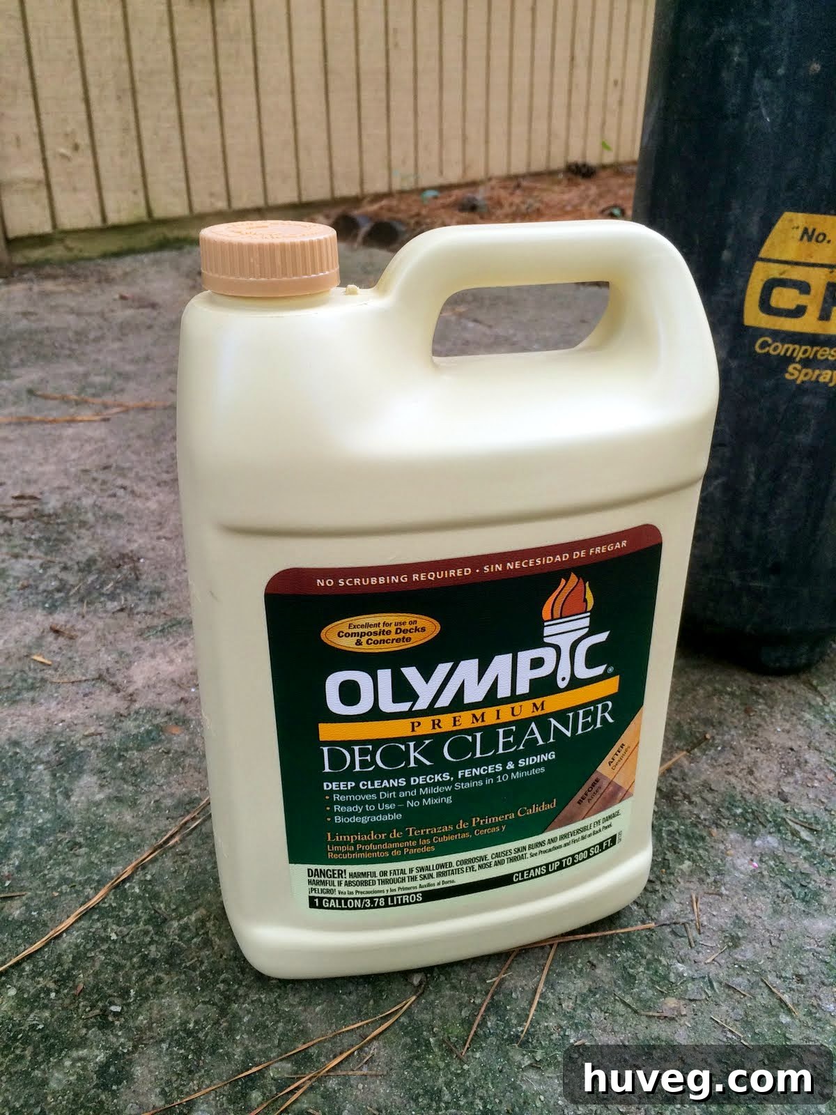 Bottle of Olympic Premium Deck Cleaner next to a garden pump sprayer