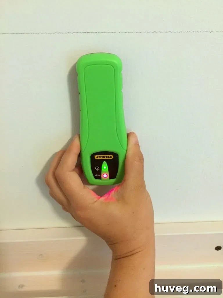 Using a stud finder to accurately mark wall studs with painter's tape before shelf installation.