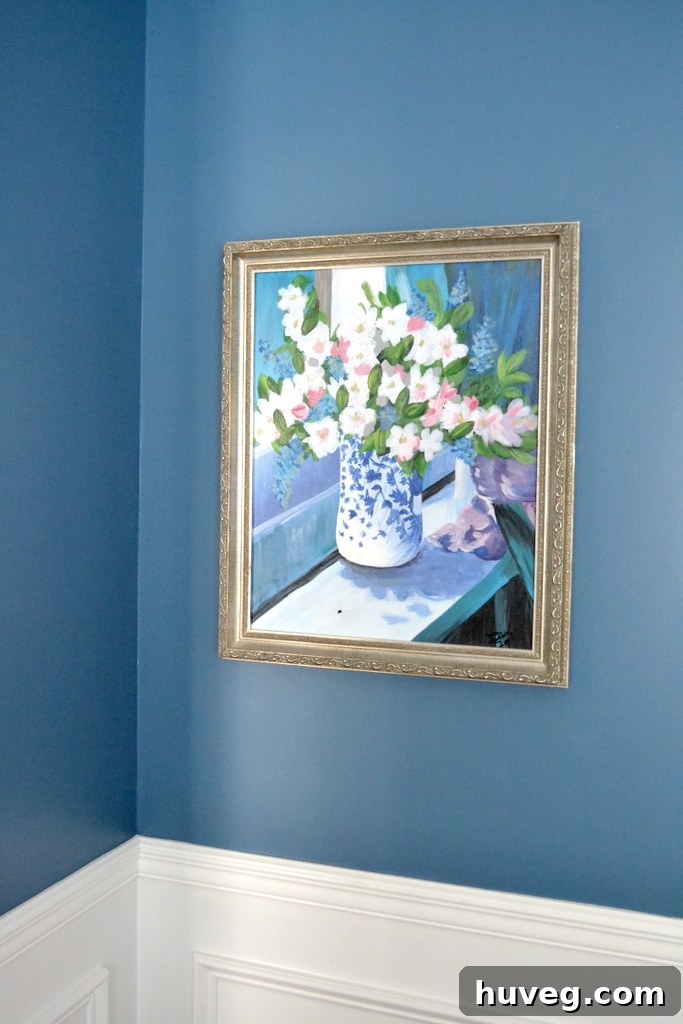 The newly hung cherished floral art piece beautifully displayed on the blue wall of the dining room, perfectly centered and illuminated.