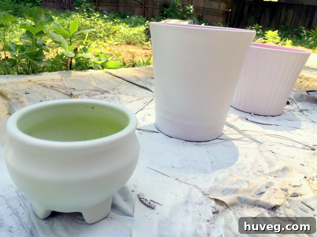 A collection of ceramic pots being spray-painted with white primer, transforming them for their new purpose.