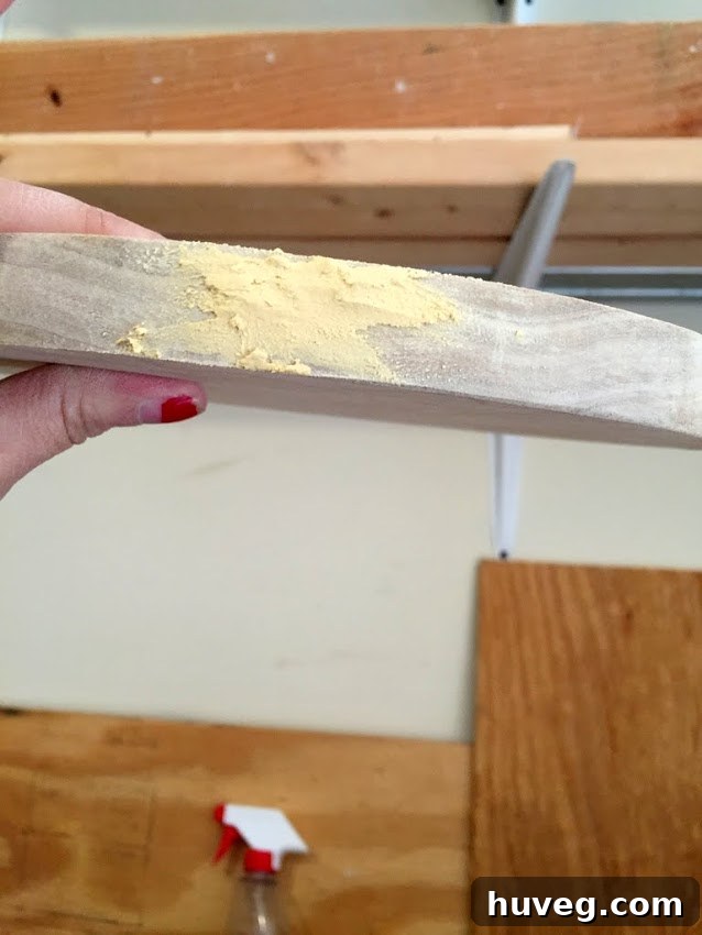 Hands applying wood filler to the edge of a round wooden piece to smooth imperfections.