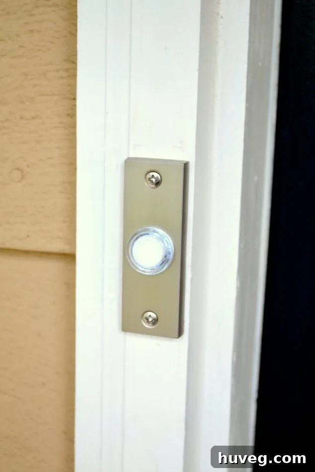 My new doorbell installed on the white doorframe next to the light brown house and navy blue front door