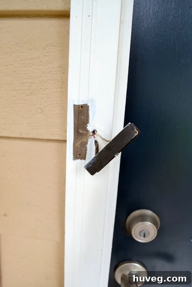 The old doorbell is off the white doorframe and hanging by wires next to the navy blue front door.