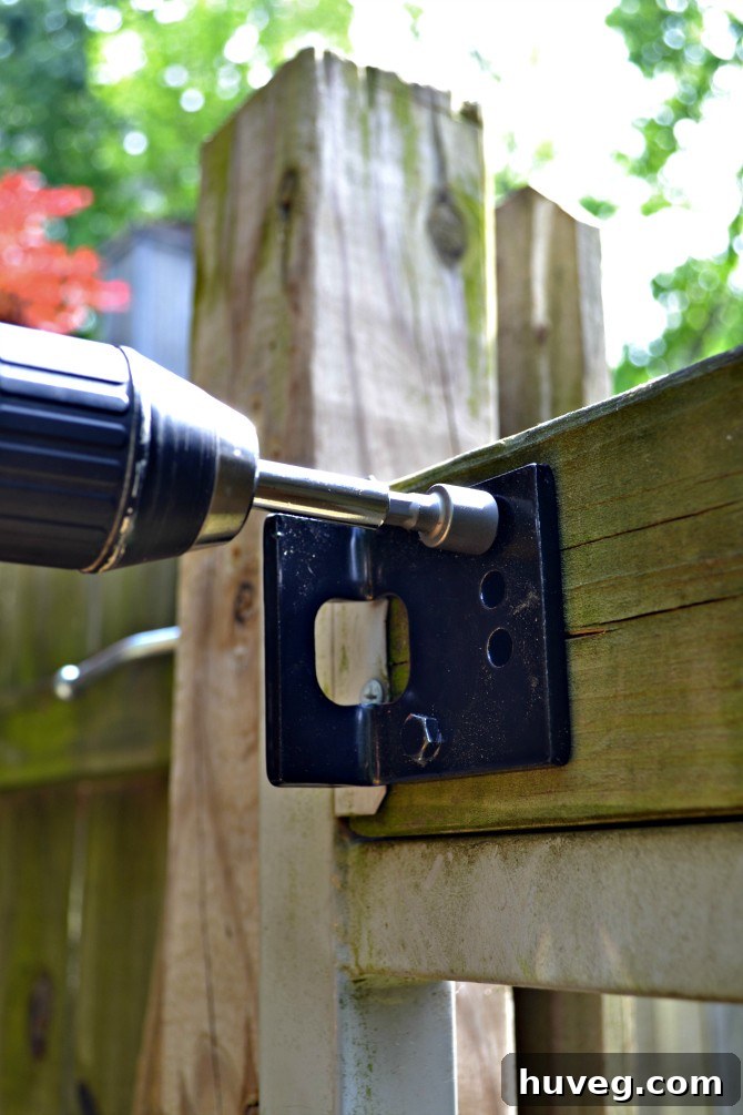 Screwing lag bolts into the gate frame using a drill with a hex nut driver bit for secure attachment